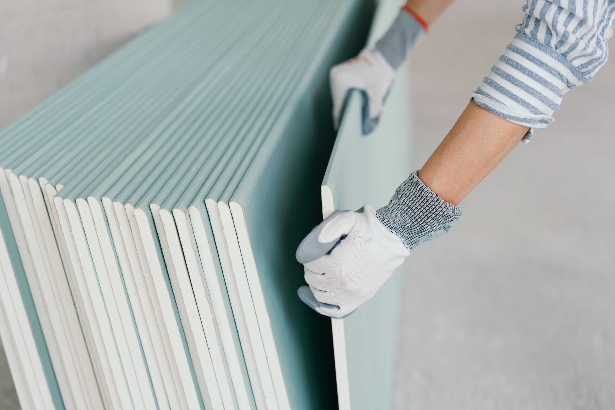Person wearing gloves taking a sheet of chip board